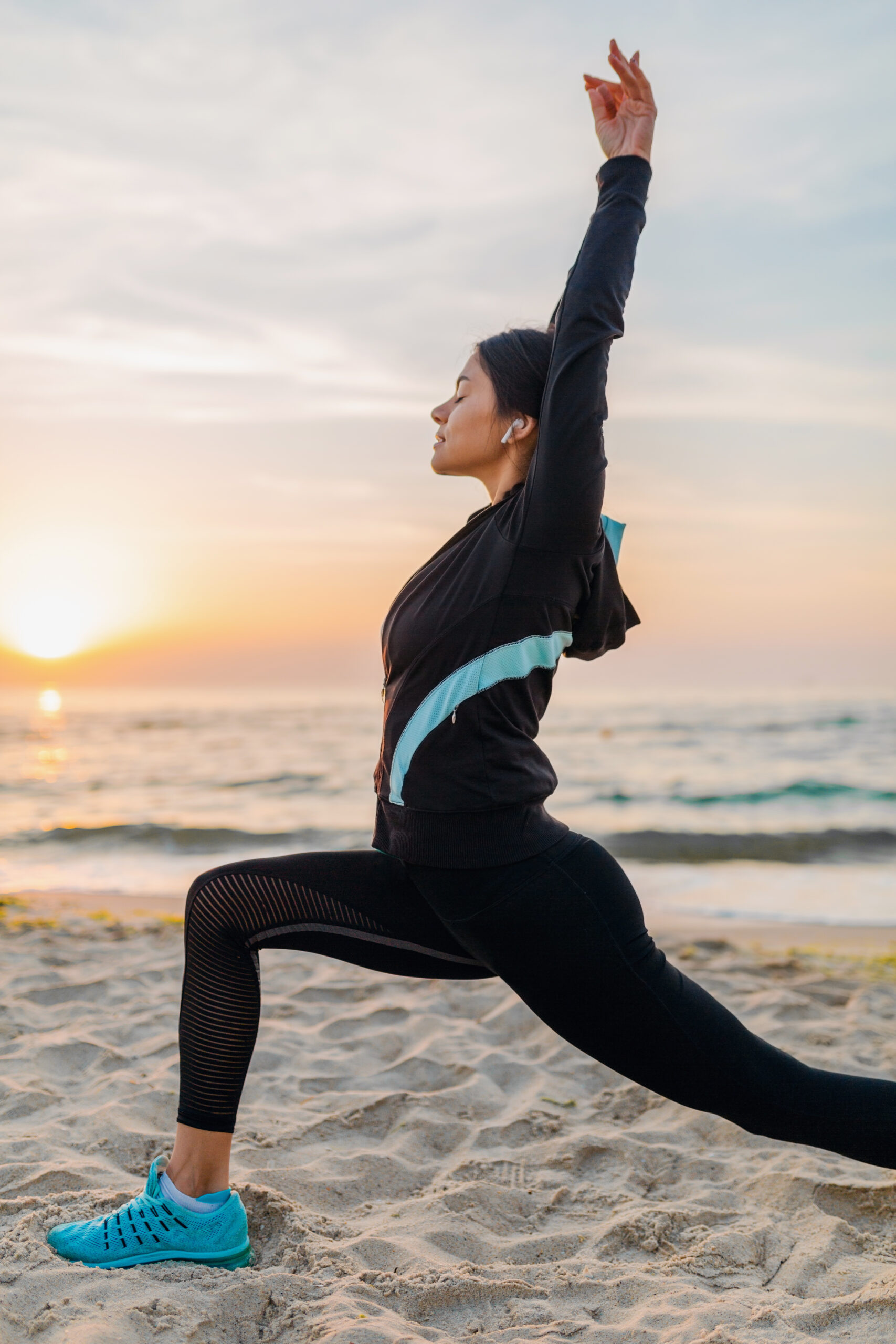 young attractive slim woman doing sport exercises on morning sunrise beach in sports wear, healthy lifestyle, listening to music on earphones, making yoga